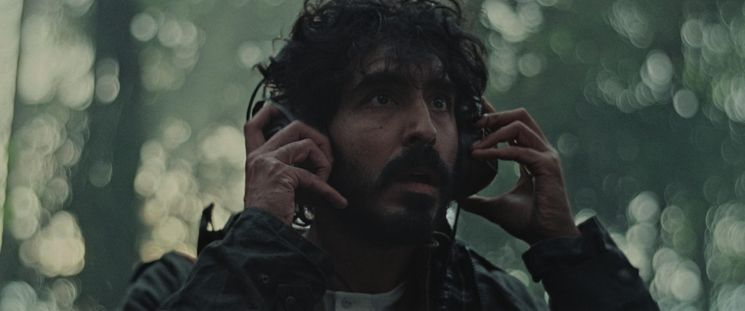 film still showing Dev Patel looking concerned with headphones on