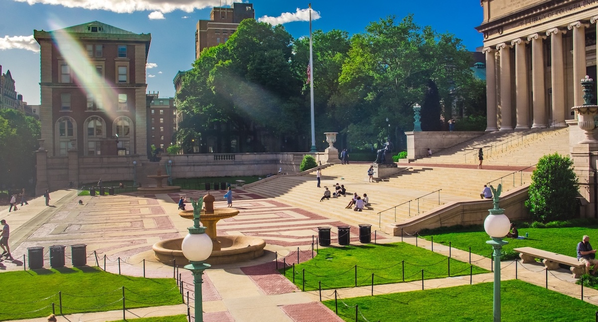 The courtyard of Columbia University on a sunny day with students sitting on the steps 