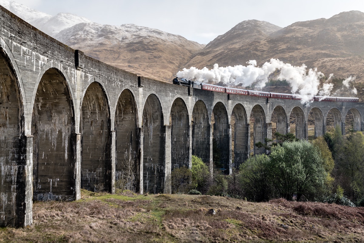 Glenfinnan Viaduct in the Scottish Highlands with steam train crossing – iconic filming location for Harry Potter and other productions