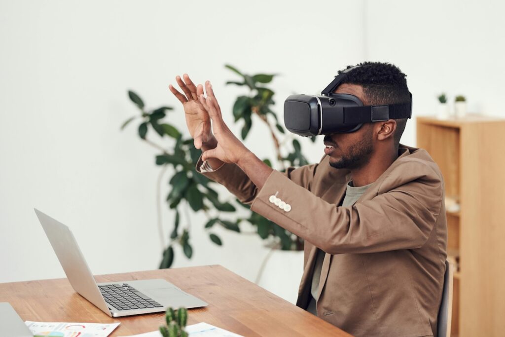an image of a man sitting in front of his laptop, wearing a Virtual Reality headset