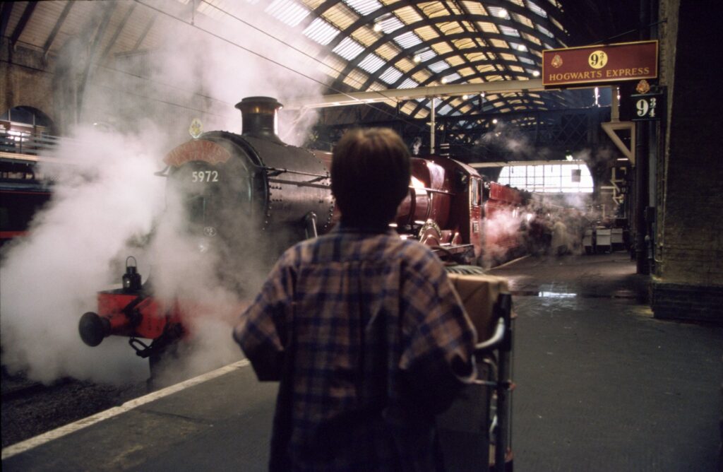 Movie still from Harry Potter and the Philosopher's Stone showing Harry at platform 9 3/4, King's Cross station