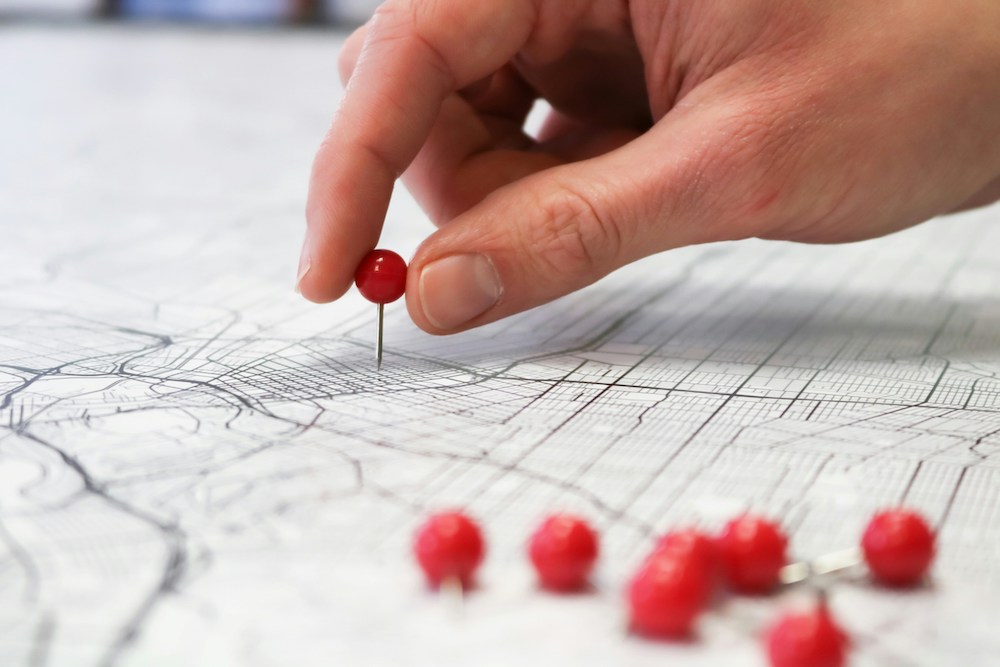 image showing a hand placing a red pin on a paper map