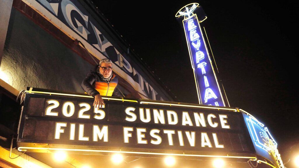 image of a man putting up a sign reading '2025 Sundance film fewstival'