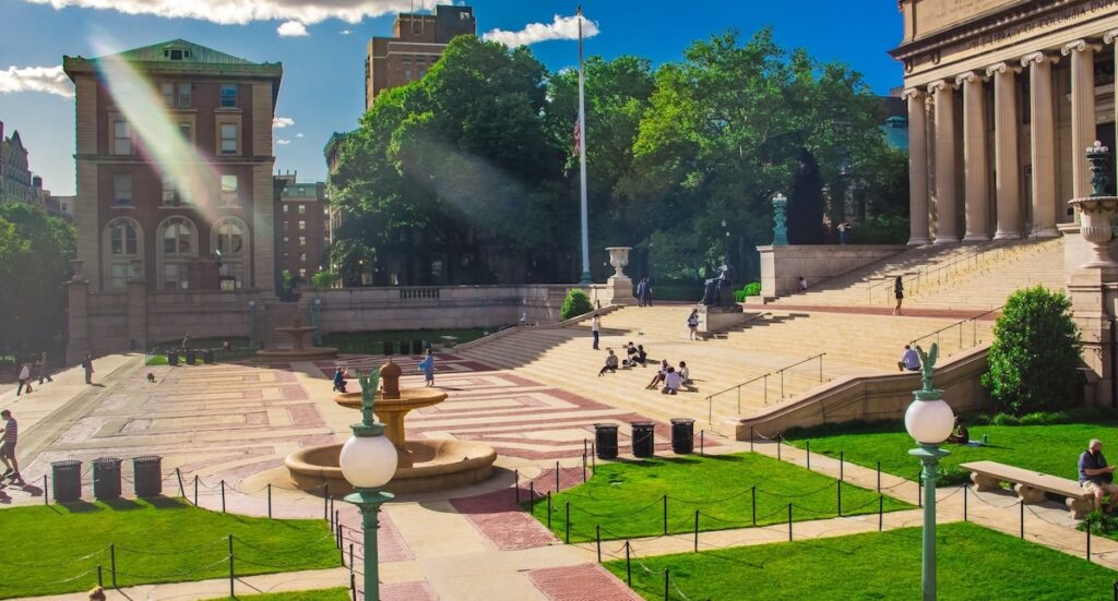 The courtyard of Columbia University on a sunny day with students sitting on the steps 