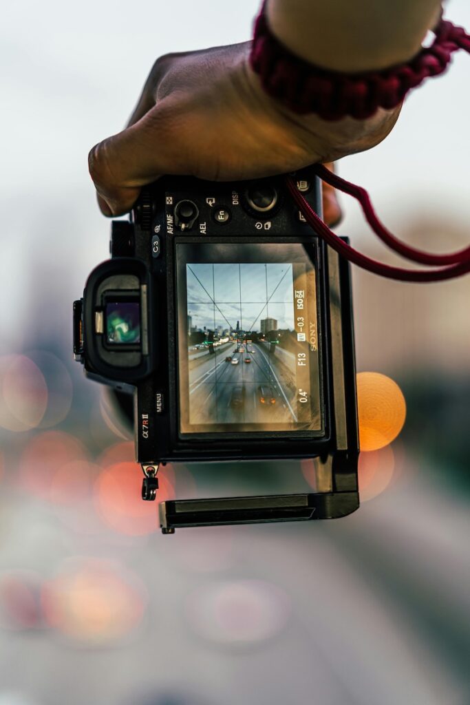 a hand holding a DSLR camera showing a road with traffic at dusk on the screen