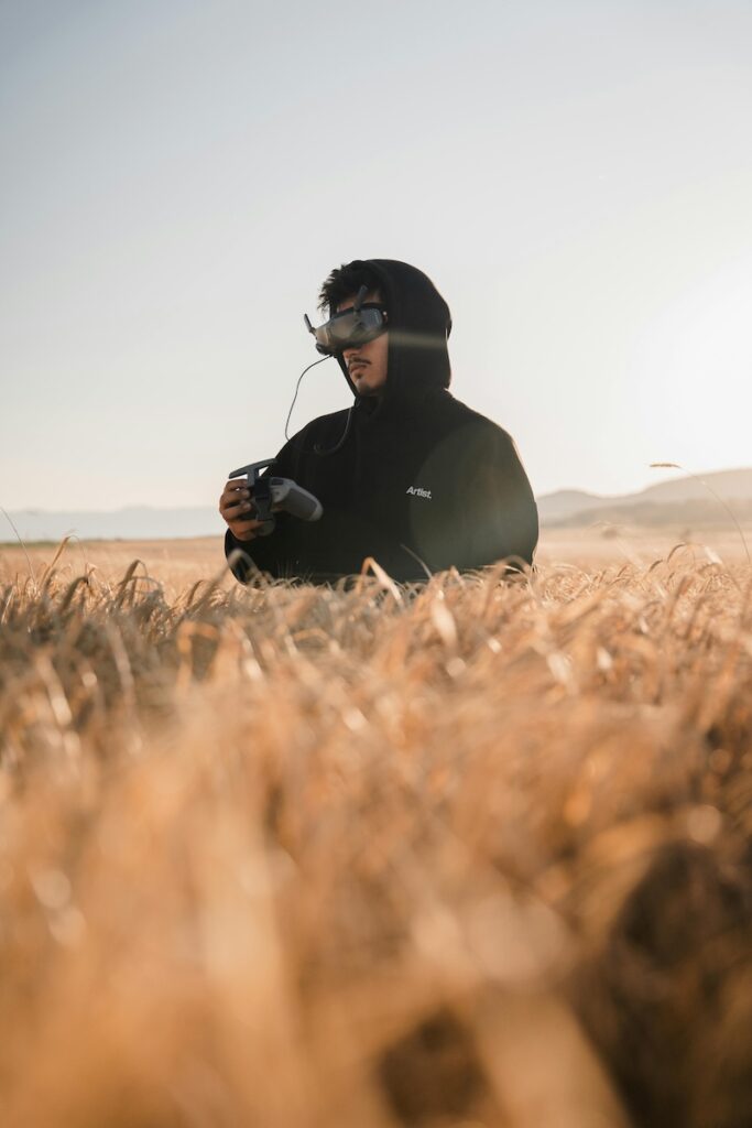 man standing in a wheat field with a headset and controller filming with a drone 