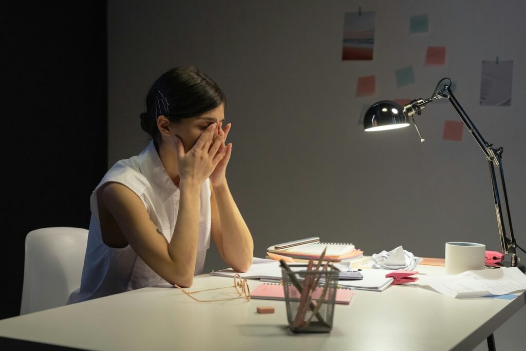 stressed businesswoman sitting at her work desk with hands covering her face