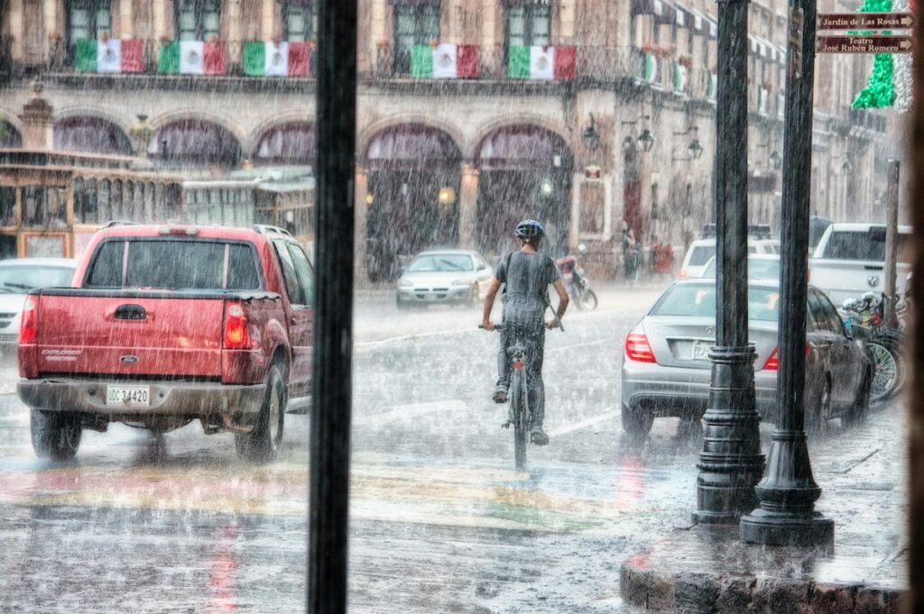 man riding bicycle down city road during heavy rain