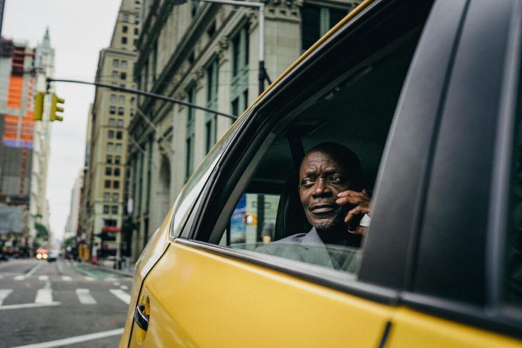 man sitting by the window of a yellow taxi driving through New York City