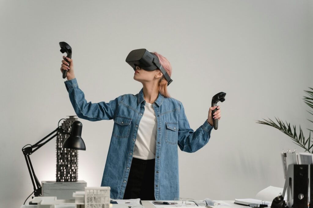 woman standing behind work desk wearing VR headset with controllers in her hands