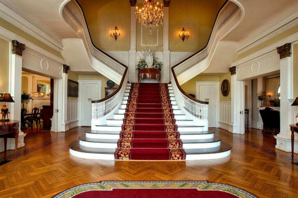 grand white staircase in entranceway with chandelier and red carpet