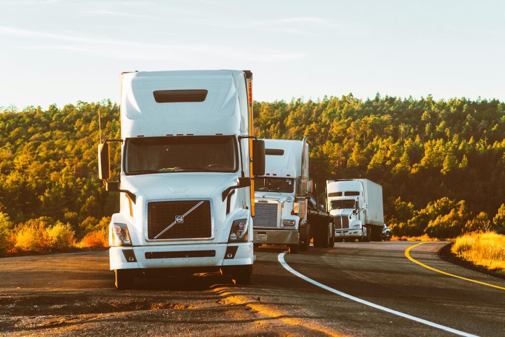 three large white trucks parked on the side of a countryside road