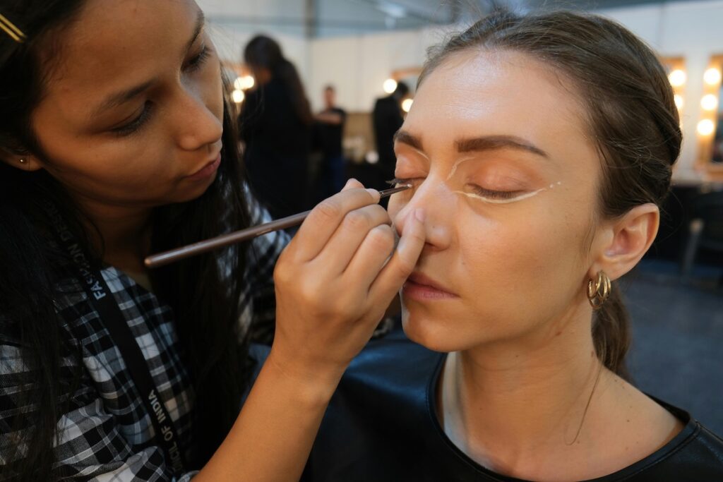 makeup artist applying makeup on a brush to a woman sitting in a large dressing room