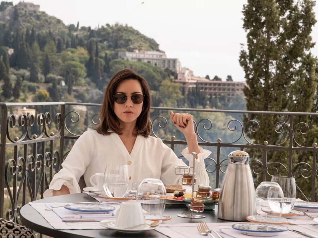 image of a White Lotus character sitting at a breakfast table on a balcony in Italy