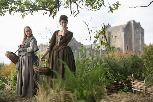Film still from Outlander (2014-) showing two female characters in a garden holding baskets