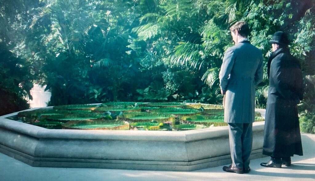Film still from House of Guiness showing two male characters staring at a pond in sefton park palm house