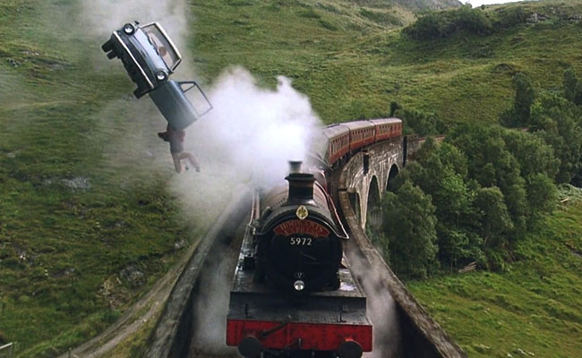 Film still from Harry Potter and the Chamber of Secrets (2002) showing Harry falling out of a flying car that is flying alongside the Hogwarts express