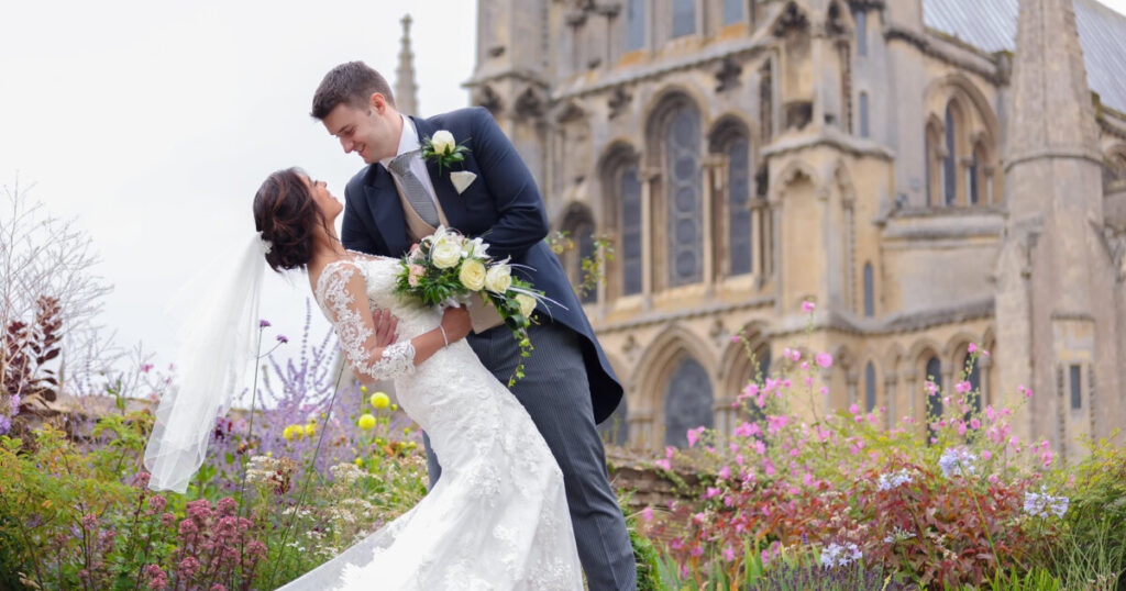 wedding photo of couple with Ely Cathedral and gardens in the backdrop 